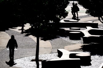 Silhouettes of people walking along a shaded path near modern architectural structures on a campus.