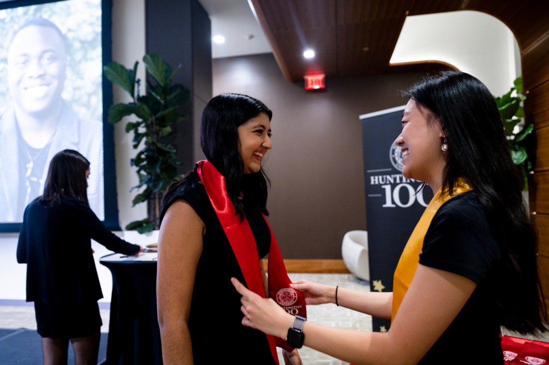 A Huntington 100 inductee wearing a yellow sash adjusting the red sash of another inductee. 