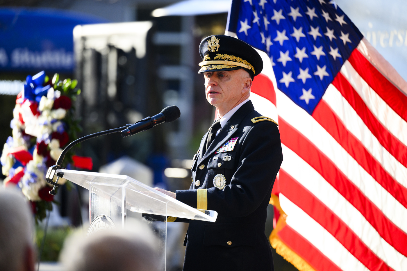 Retired Brigadier General John J. Driscoll speaking at a podium outside next to a US flag.