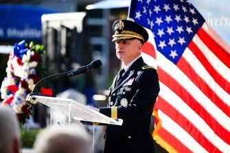 Retired Brigadier General John J. Driscoll speaking at a podium outside next to a US flag.