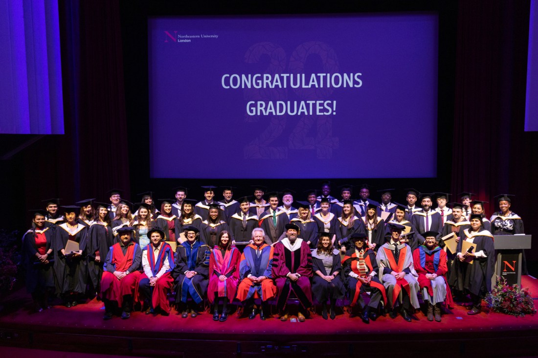 Graduates posing for a group photo in front of a screen that says 'Congratulations Graduates!' on it.