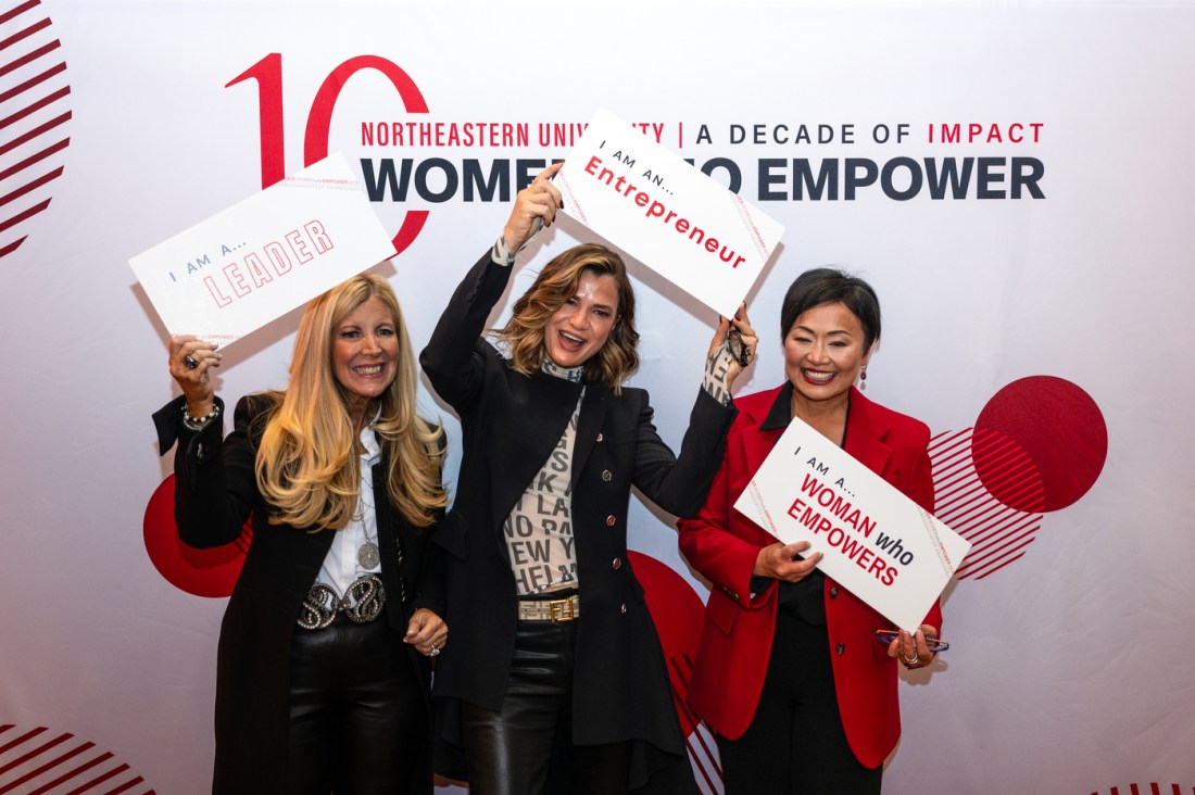 Three people posing in front of a Women Who Empower backdrop.