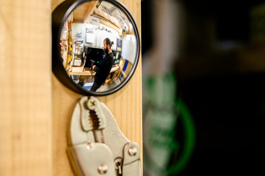 Reflection of a person working in a workshop, captured through a convex mirror.