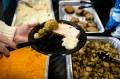 A person scooping brussel sprouts onto a plate with other Thanksgiving foods.