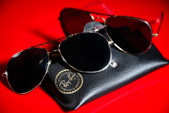 Dupe product of Ray Ban sunglasses displayed on a case against a red background.