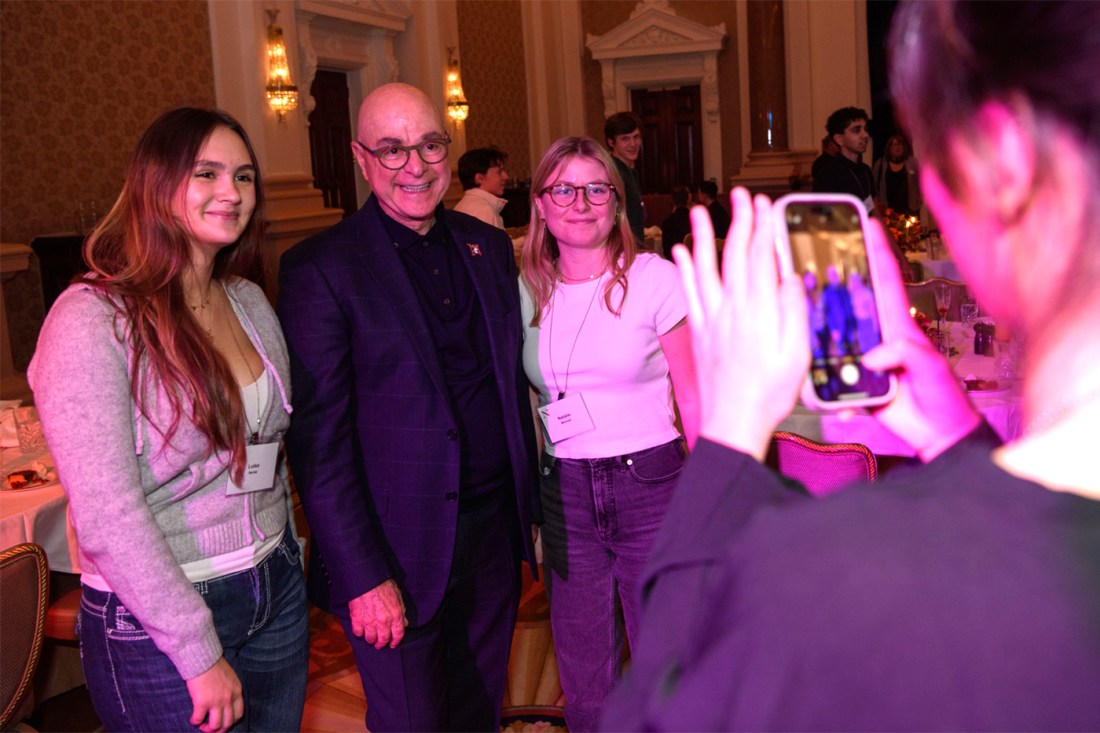 Joseph E. Aoun poses for a photo with two students while another takes a picture with a phone.