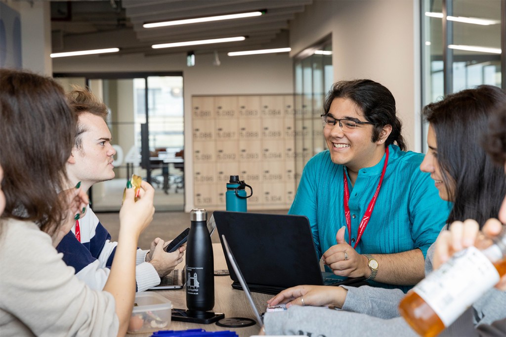 A group of students collaborates and works together in a shared workspace.