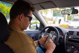 A person sits in a car interacting with a device.