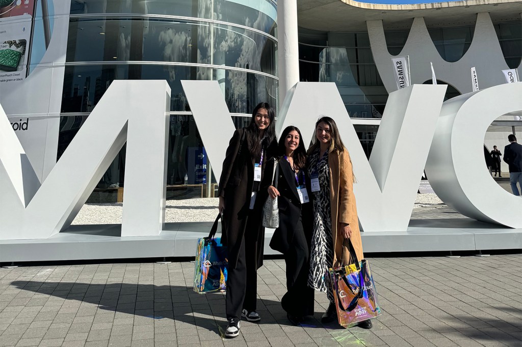 Three people stand in front of large event signage outdoors.