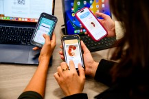 Three people's hands with their phones open to various pregnancy apps.