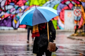 A person with a blue and white umbrella walks past a colorful mural near a koi pond.