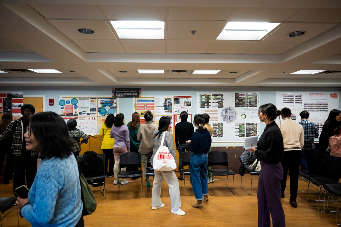 Students milling about a room looking at pojects printed out on paper and hung around a room.