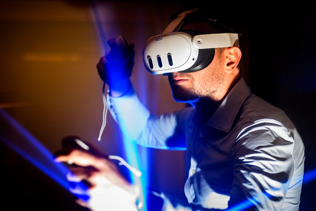 A person wearing a virtual reality headset, holding controllers, with blue light beams in the background.