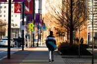 A person walks along a sidewalk carrying a large bag, with trees and campus banners lining the path.