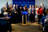 A group of people standing behind Governor Healey as she speaks at a podium at the AI announcement.