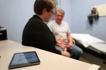 A health care professional talking with a patient. An iPad sits on a desk next to them.