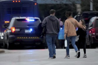 Three people walking outside of a school in Wisconsin by a police car with it's lights on.