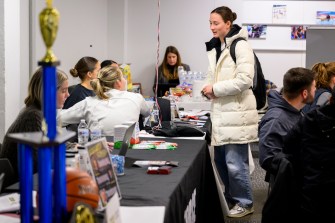 A student in a white puffer jacket stnading at a table during the Athletics co-op fair.