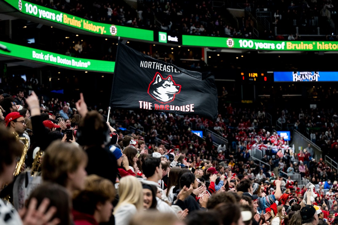 A black flag with a husky on it that says 'Northeastern The Dog House' waves above the Northeastern student section 