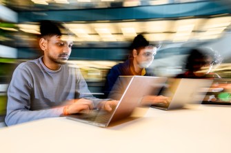 A blurred photo, to emulate motion, of people typing on their laptops.