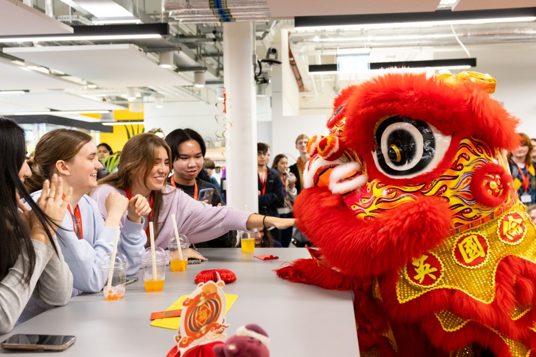 A person in traditional Chinese dragon costume sitting across the table from a group of students.