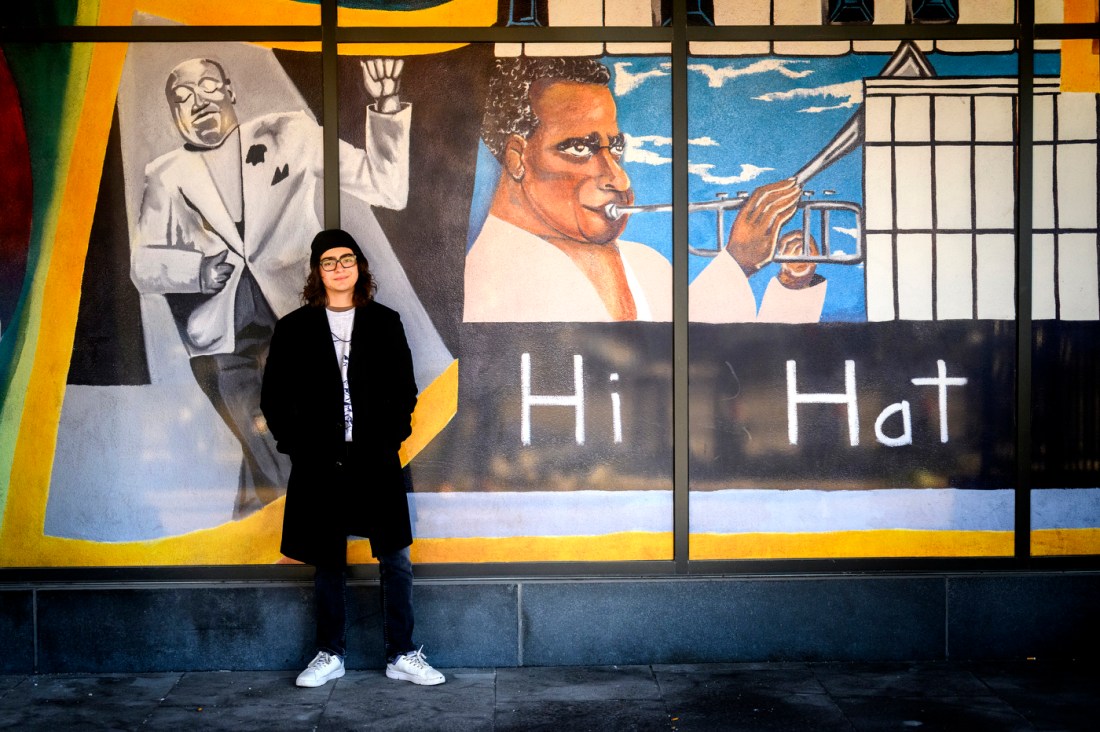 Andres Garcia standing in front of a mural of jazz artists. 