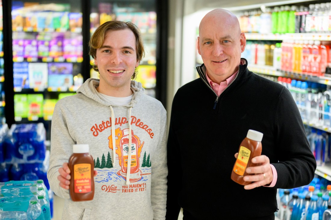 Jack Burns wearing a hoodie that says 'Ketchup Please' on it holding a bottle of ketchup while standing next to another guy holding a bottle of ketchup.