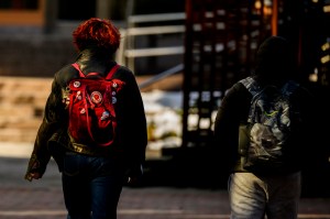 Two students seen from behind as they walk across campus wearing backpacks.