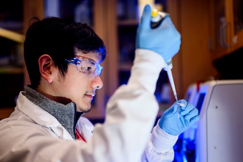 Researcher in a lab coat and safety goggles carefully uses a pipette to prepare a sample in a laboratory setting.