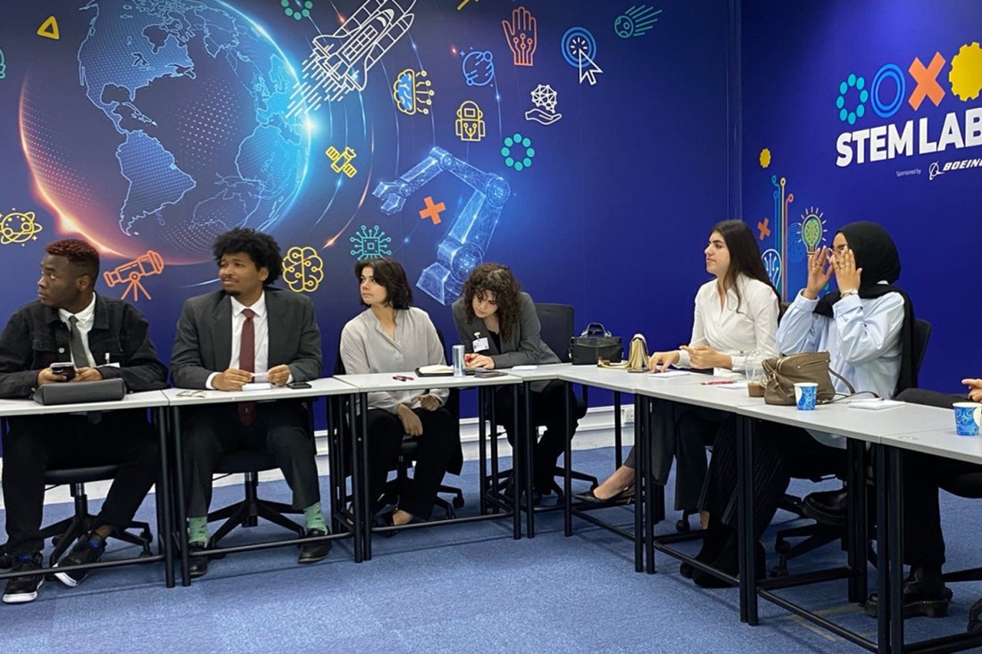 A group of people sitting around a square table in front of a backdrop that says 'Stem Lab' on it.