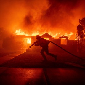 A firefighter carrying a hose in front of a burning home in California.