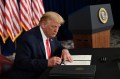 President Trump signing a piece of paper at a desk with US flags hanging behind him.