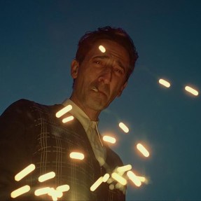 A screen capture of a character at night looking down at the camera as sparks fly across the screen.