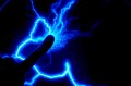 A finger touching a dark surface. Where the finger is touching, blue sparks and bolts of energy appear around it.