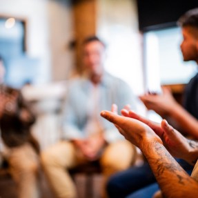 A close up of a person applauding while sitting in a circle with a support group.