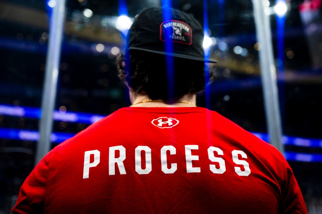 A mens hockey player wearing a backwards hat and a red t-shirt that says 'PROCESS' on the back.