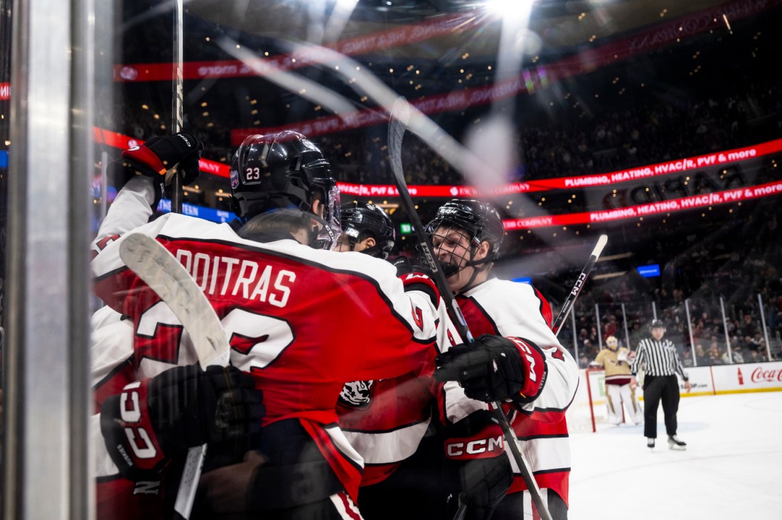 Northeastern hockey players grab each other and cheer in a huddle after scoring a goal.