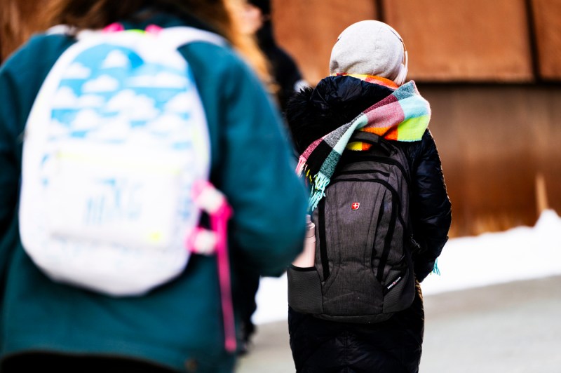 People walk on a pedestrian bridge, wearing backpacks and winter clothing.