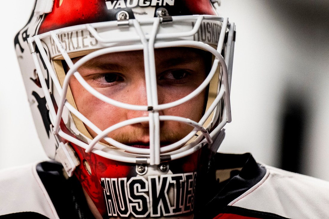 Close-up of a hockey player wearing a helmet and red-and-white uniform, looking focused and ready for the game.