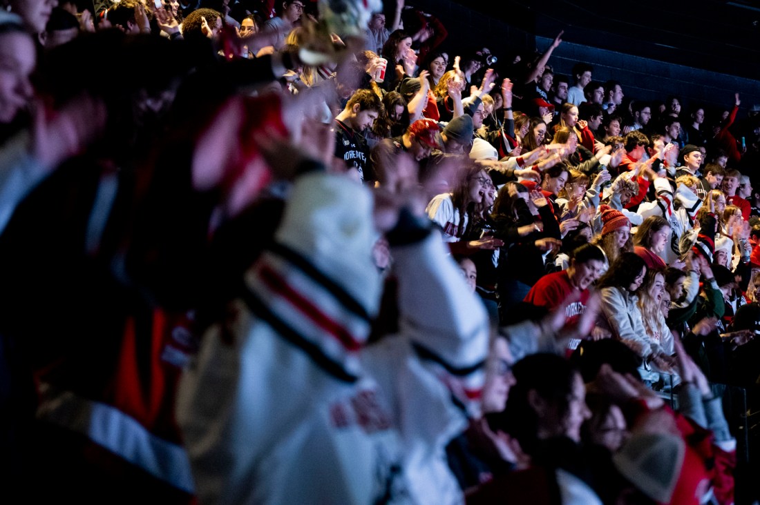 A crowd of energetic fans in a stadium, many wearing team colors and cheering enthusiastically.