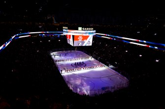 Northeastern and Boston College players stand in two lines on the ice at TD Garden. The rink is dark, but the ice is lit up. The jumbotron has Boston College's and Northeastern's logos on the screen.