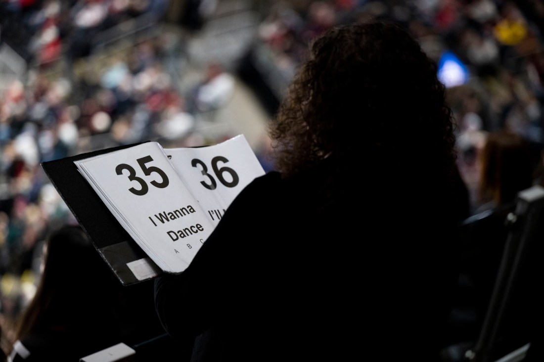 A close-up of a music sheet with "I Wanna Dance" visible, held by a member of Northeastern's pep band at the Beanpot semifinal.