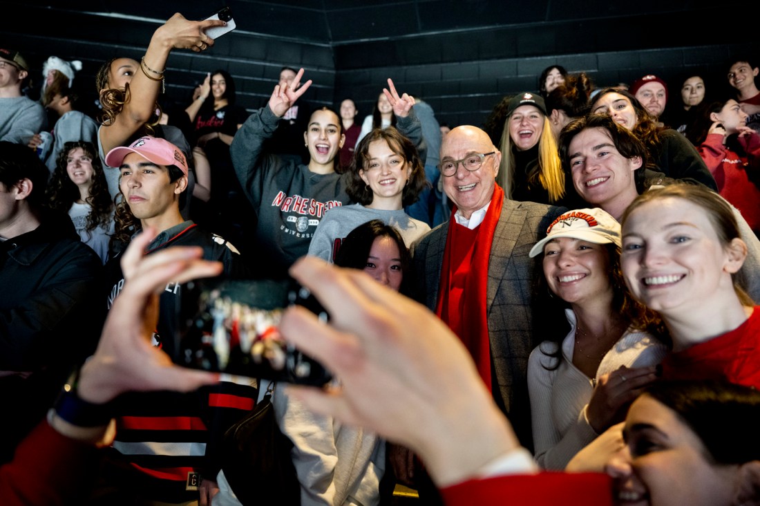 A person's hands taking a horizontal photo of Northeastern President Aoun at TD Garden surrounded by students.