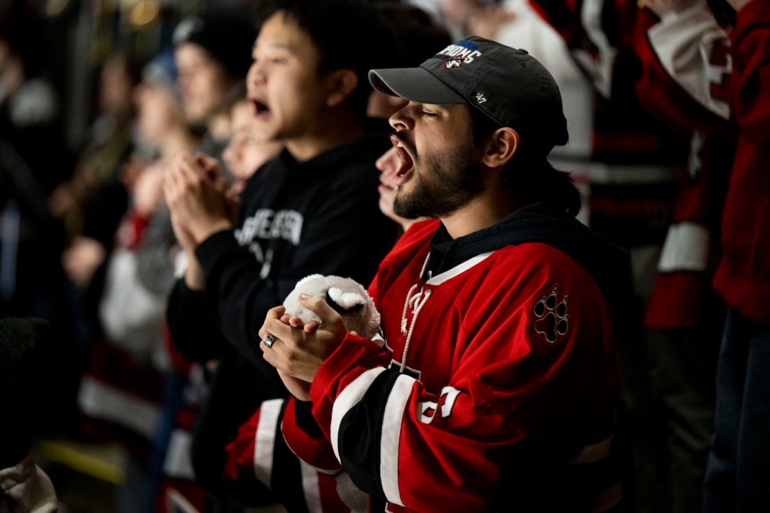 Fans in the stands, some wearing Northeastern gear, enthusiastically clapping and cheering.