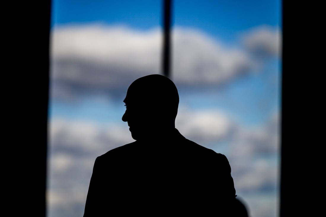 Silhouette of an attendee at a conference standing in front of a window. Outside, there is blue sky and clouds. 