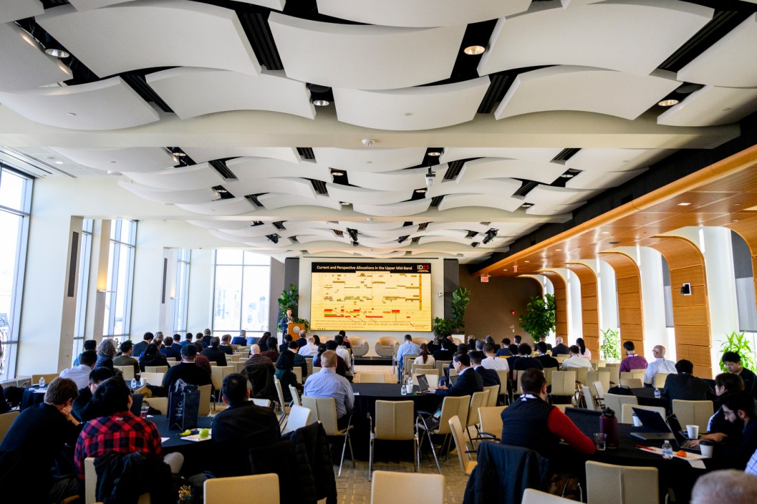 A room full of audience members with curved panels on the ceiling.