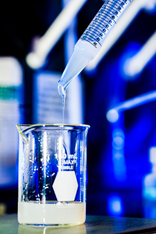 A close up of a syringe dripping a liquid into a beaker.