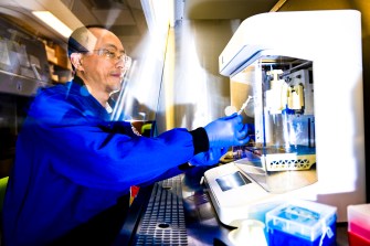 Guohao Dai wearing a blue lab coat and blue lab gloves working in a lab.