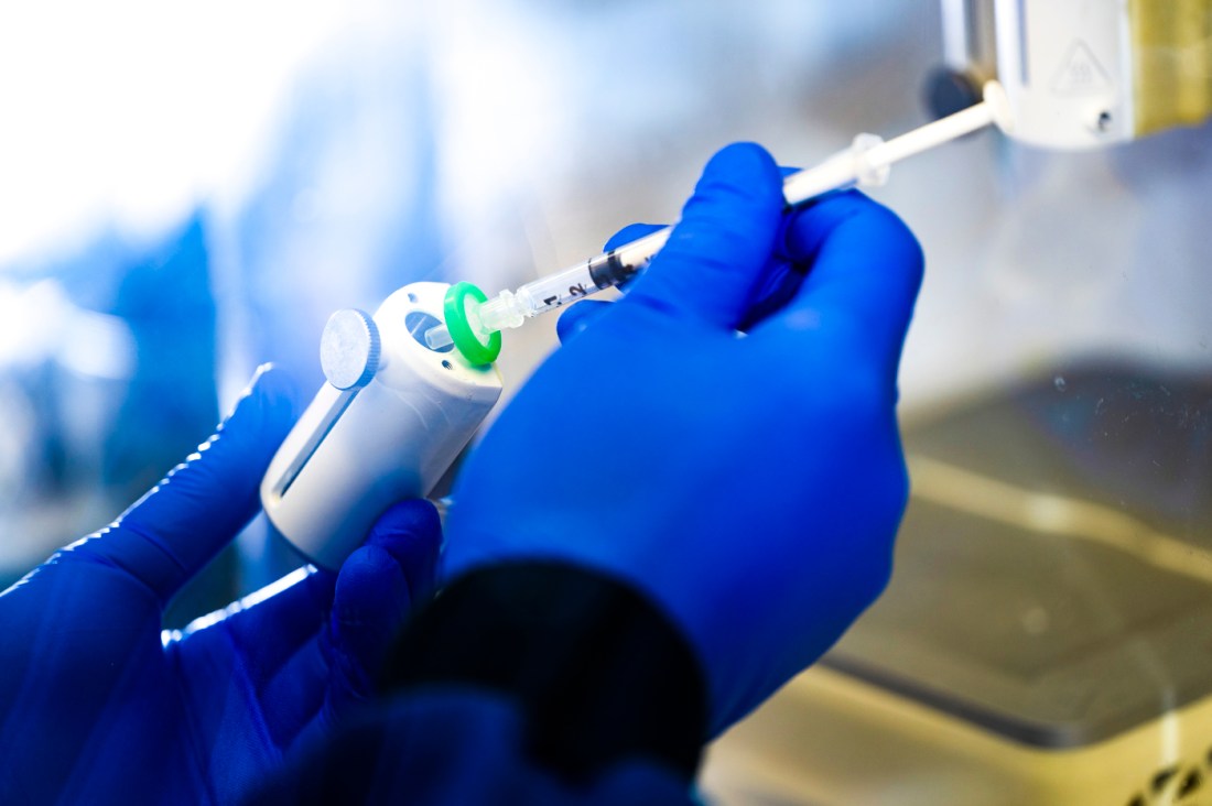 Guohao Dai's hands in blue lab gloves while he fills a syringe. 