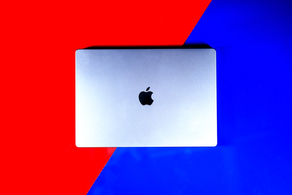 A MacBook laptop on a background which is divided diagonally and red at the top left and in blue at the bottom right.